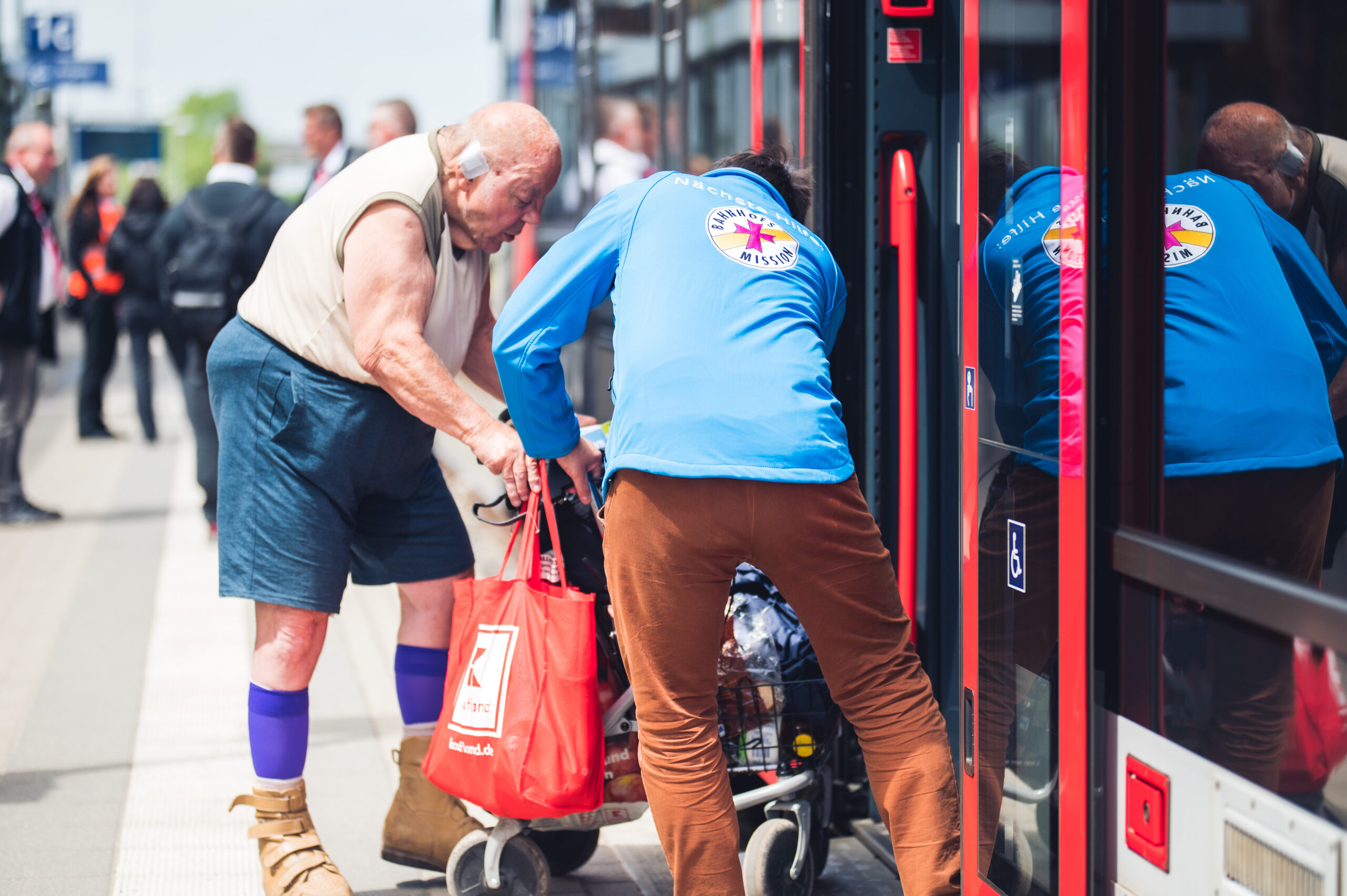 Rollator-Fahrer steigt in den Zug ein. Ein Mitarbeiter der Bahnhofsmission hilft ihm.